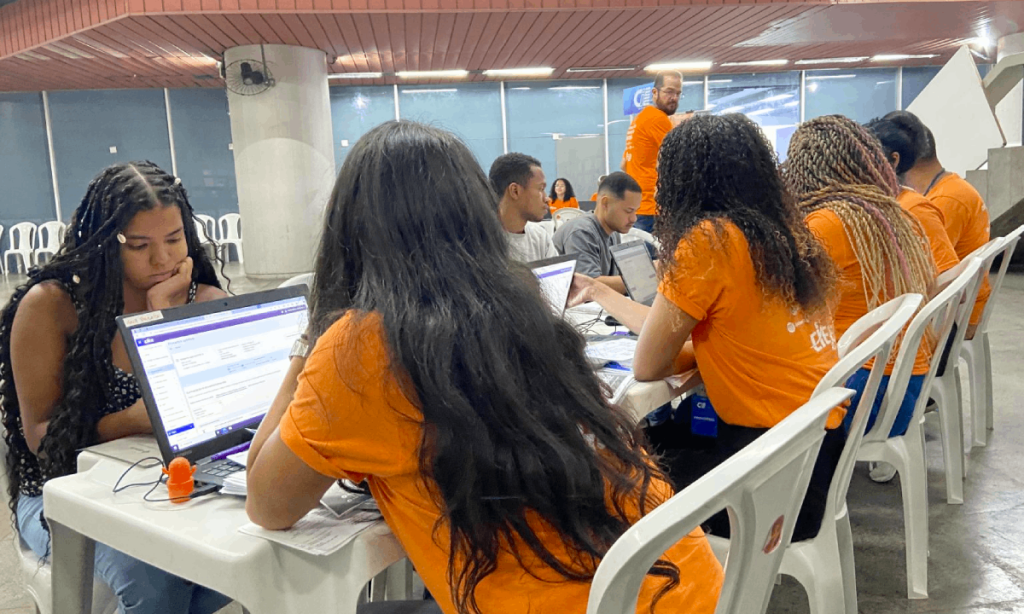 Estudantes sentados em fila de atendimento no estande do CIEE Rio dentro da estação de metrô Maracanã. Ao fundo, banners com informações sobre vagas de estágio e jovem aprendiz.