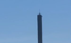 Imagem do obelisco, da Ponte Rio-Niterói, com homem tentando roubar cabos, durante o dia.