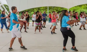Grupo de pessoas praticando aula de dança ao ar livre na área de eventos do Parque RJ Nosso Sonho, no bairro Boa Vista, em São Gonçalo, sob a luz do dia.
