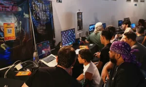 Jovens sentados jogando jogos eletrônicos em computadores enquanto outros assistem