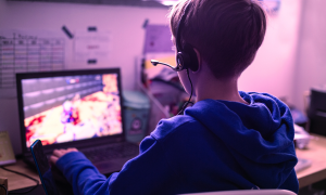 Criança sentada jogando jogo eletrônico em frente a um computador