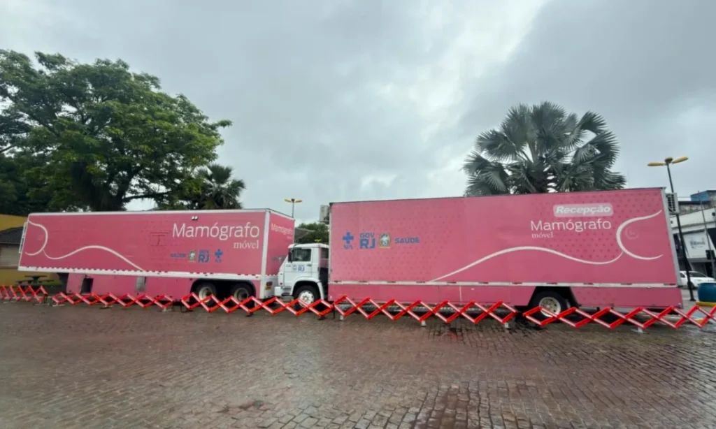 Dois caminhões rosas, de mamografo movel, estacionados frente a frente.