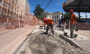 Operários da Prefeitura de Niterói trabalhando na calçada em vias próximas à Amaral Peixoto, no Centro. Há cones de sinalização laranja delimitando uma faixa da via e pedestres caminhando ao fundo.