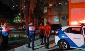 Fachada da 78ª Delegacia de Polícia no Fonseca, Niterói, com viaturas da Polícia Militar estacionadas na frente durante o entardecer.