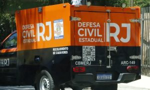 Foto de viatura do Corpo de Bombeiros com luzes acesas estacionada à noite em rua residencial de São Gonçalo, com escombros de construção ao fundo.
