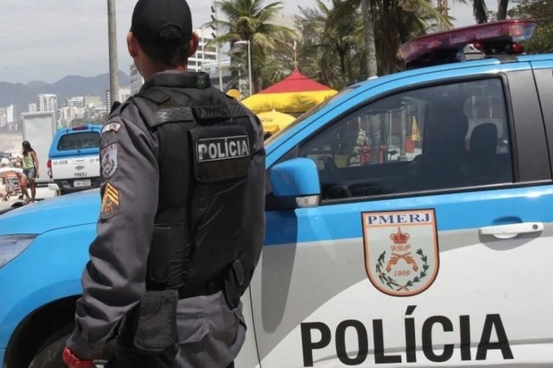 Fotografia de viatura da Corregedoria da Polícia Militar do Rio de Janeiro estacionada durante operação contra policiais militares envolvidos com milícia. Ao fundo, prédios urbanos sob luz do dia.