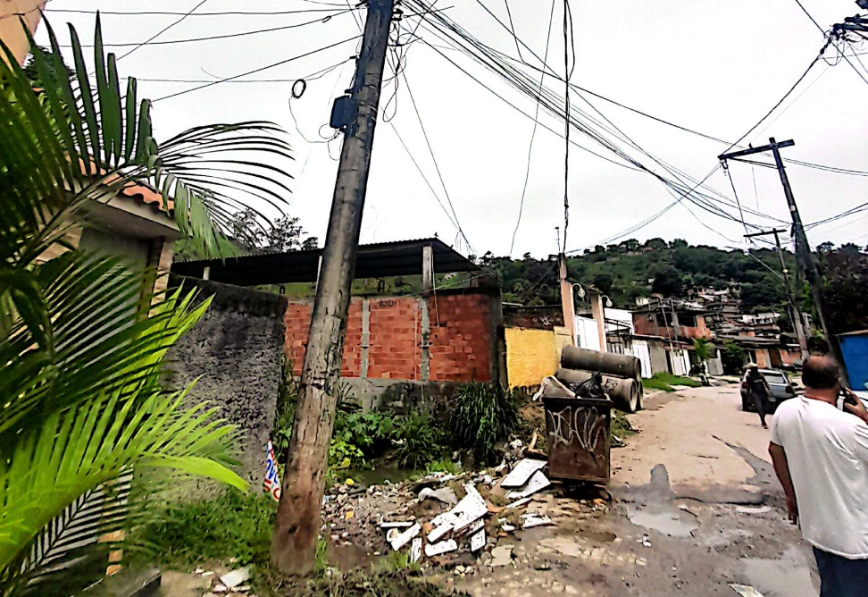 Poste de energia elétrica visivelmente inclinado em via pública, localizado em área residencial da comunidade da Coruja, em São Gonçalo.