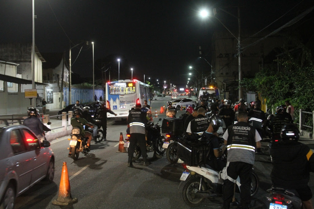 Agentes da Secretaria de Meio Ambiente e Transportes e policiais realizam operação de trânsito, abordando motociclistas em via pública.