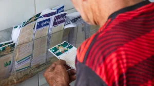 Loterias da Caixa terão dia de sorteio alterados. Na imagem, homem de camisa vermelha com volante de aposta nas mãos.