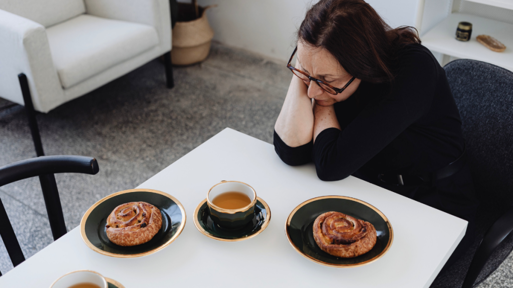 Mulheres com dificuldade para emagrecer. Na foto, mulher triste sob a mesa com cafés e pães
